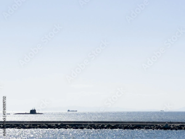 Fototapeta A submarine on the surface of the ocean with sparkling seas and a lighthouse in the foreground
