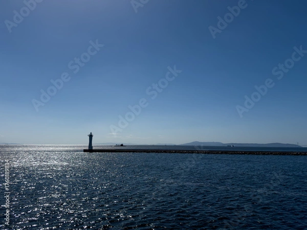 Fototapeta A submarine on the surface of the ocean with sparkling seas and a lighthouse in the foreground