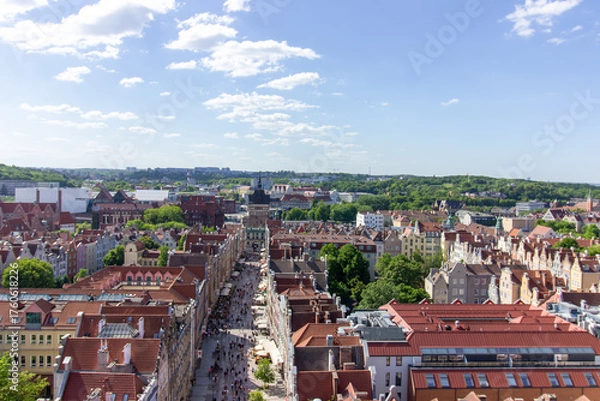Fototapeta Aerial panoramic view of the historic Old Town of Gdańsk, Poland, with red tiled rooftops, bustling pedestrian street, and surrounding green landscape on a sunny summer day