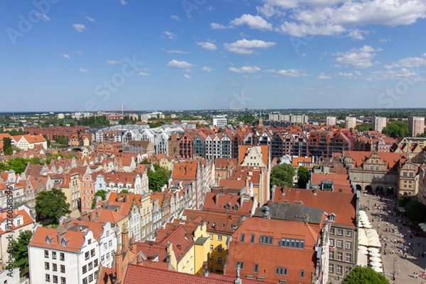 Fototapeta Aerial panoramic view of the historic Old Town of Gdask, Poland, with red tiled rooftops, bustling pedestrian street, and surrounding green landscape on a sunny summer day