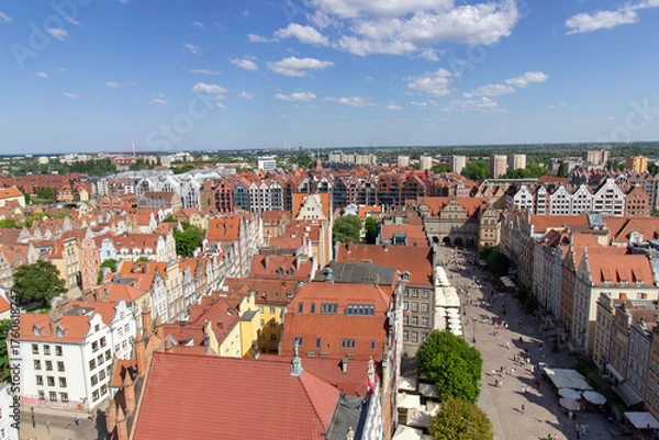 Fototapeta Aerial panoramic view of the historic Old Town of Gdask, Poland, with red tiled rooftops, bustling pedestrian street, and surrounding green landscape on a sunny summer day