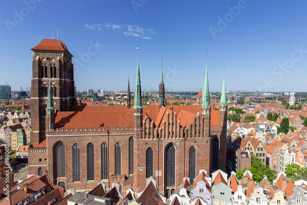 Fototapeta Aerial panoramic view of the historic Old Town of Gdask, Poland, with red tiled rooftops, bustling pedestrian street, and surrounding green landscape on a sunny summer day