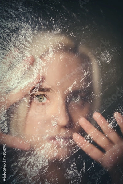 Fototapeta Woman looking scared through hole in transparent plastic curtain, scared and alone in dark