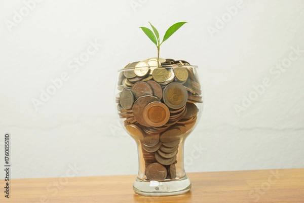 Fototapeta A small green plant growing from a glass full of coins symbolizes financial growth, investment, savings, and sustainable wealth. Perfect for business, finance, or eco investment concepts.