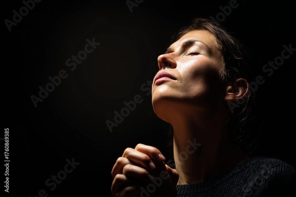 Fototapeta Woman praying in darkness with hopeful expression