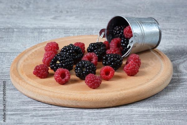 Fototapeta The natural fresh raspberry and blackberry on the wooden plate with a decorative metallic bucket.