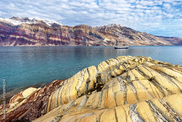 Fototapeta The amazing colourful rock formations of Segelsalskapet fjord, in the Northeast Greenland National Park. A tall sailing ship and the Berzelius Bjerg Mountain can be seen behind.