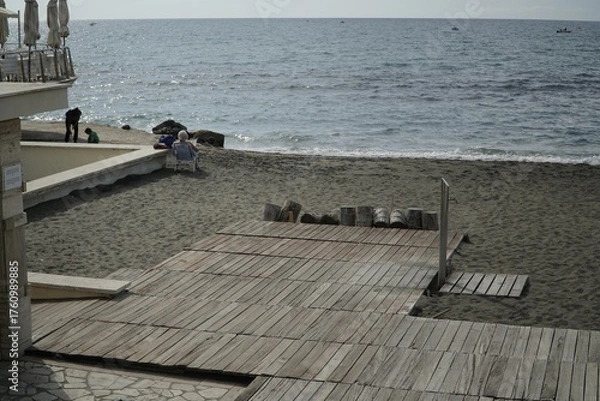 Fototapeta Ostia, Rome, Italy - October 19, 2025, a lady from behind sunbathes on the beach on a folding chair on a beautiful October day, called ottobrate romane in Rome.
