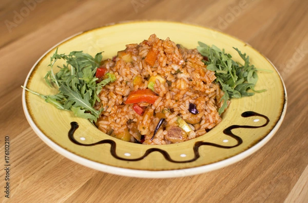 Fototapeta A plate of rice with vegetables. Appetizing healthy rice with vegetables in white plate on a wooden background.