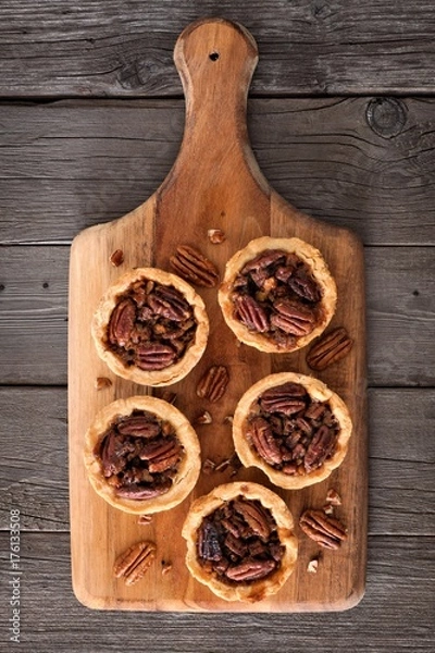 Fototapeta Mini pecan pie tarts on a wooden paddle board against a rustic wood background