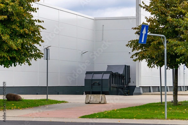 Fototapeta Waste container next to back wall of building, concrete barrier and traffic sign, facility service area, garbage storage point, industrial surroundings