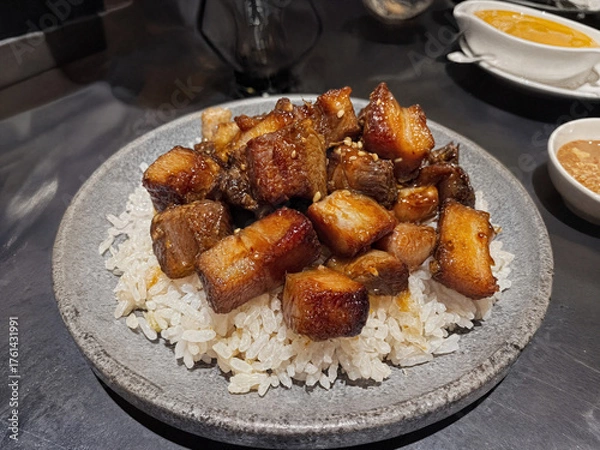 Fototapeta A popular Filipino dish featuring succulent, caramelized pork belly chunks served over fragrant garlic rice, creating a perfect blend of savory and slightly sweet flavors.