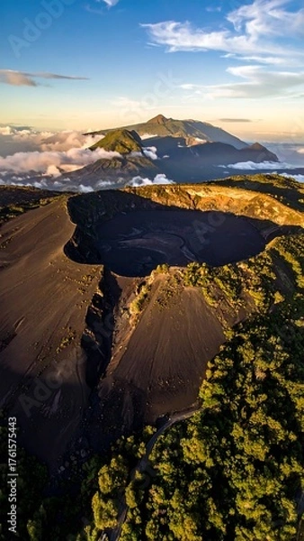 Obraz Aerial view of a large volcanic crater and mountainous terrain under a partly cloudy blue sky during golden hour