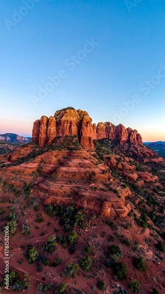 Fototapeta Aerial view of a striking red sandstone formation under a vibrant, clear blue sky during dusk, casting golden hues