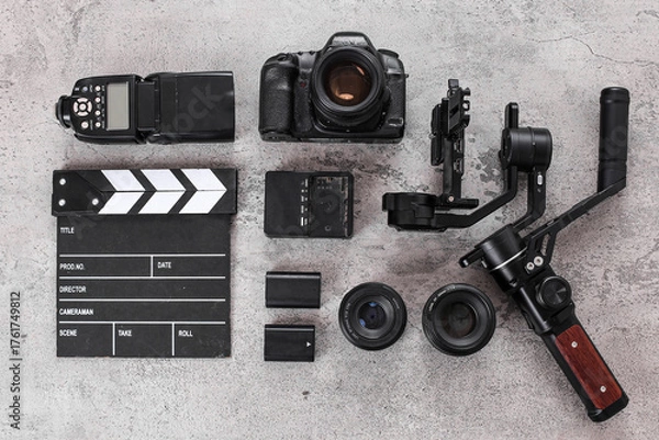 Fototapeta Flat Lay Of Filmmaker Gear With Camera, Gimbal, Clapperboard, Lenses, Flash Over Cement Background
