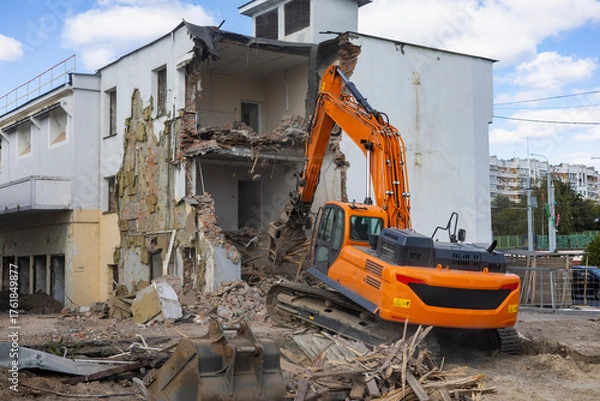 Fototapeta Heavy machinery demolishes building structure during construction project in urban area