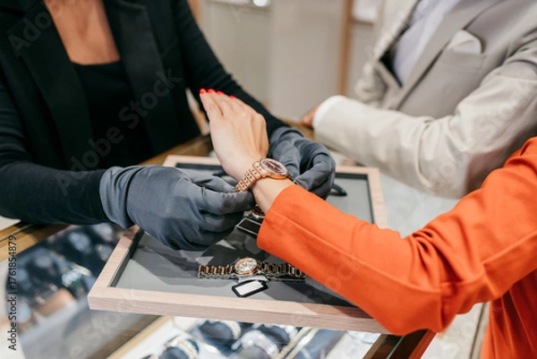 Fototapeta Sales associate in protective gloves assisting a customer with trying on an elegant wrist watch in a luxury jewelry store, offering specialized retail service