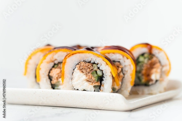 Fototapeta Sushi roll with salmon,  avocado and tuna. Sushi set served on the white plate next to red ginger with wooden sticks on the white background