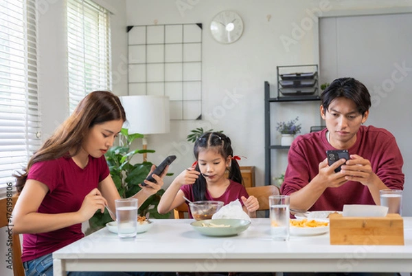 Fototapeta Family members sitting at dining table, focusing on their mobile phones instead of interacting during lunch