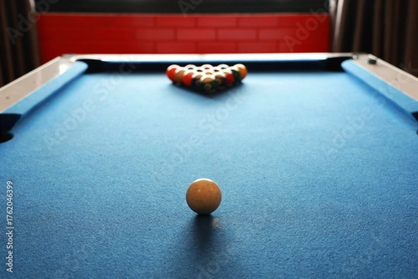 Fototapeta A white ball is placed in the center of the pool table. The balls are arranged in a pyramid for hitting. A blue billiards table has a blur of colorful balls. Billiard balls with numbers on pool table
