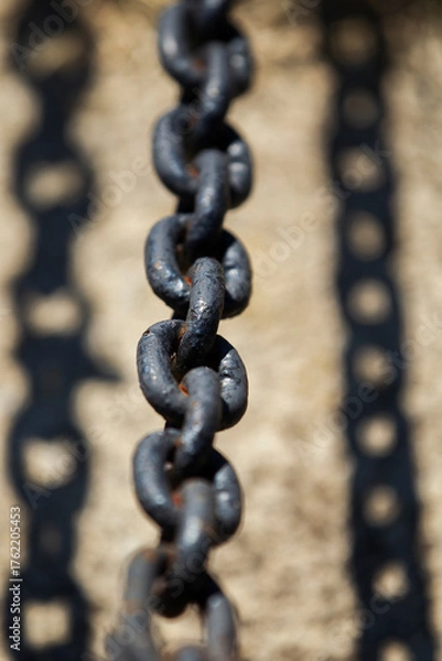 Fototapeta Close-up of dark metal chain casting shadow on concrete. Industrial chain with strong sunlight and sharp shadow.