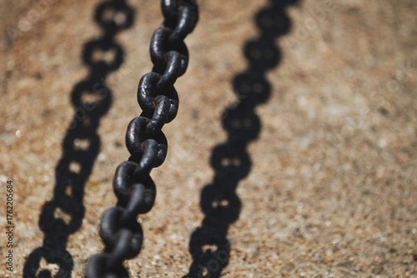 Fototapeta Close-up of dark metal chain casting shadow on concrete. Industrial chain with strong sunlight and sharp shadow.