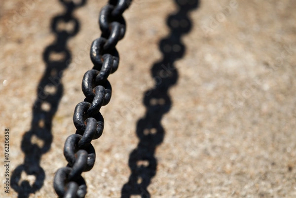Fototapeta Close-up of dark metal chain casting shadow on concrete. Industrial chain with strong sunlight and sharp shadow.