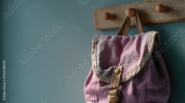 Obraz Pink backpack hanging on a wooden coat rack against a blue wall. the backpack is made of a textured fabric with a purple and white striped pattern.