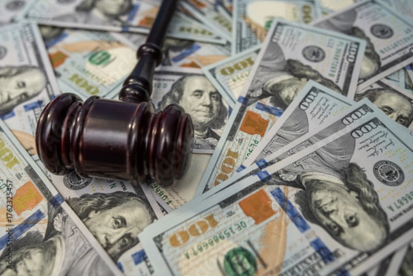 Fototapeta Judge's gavel resting on scattered US 100 dollar bills, symbolizing financial law.