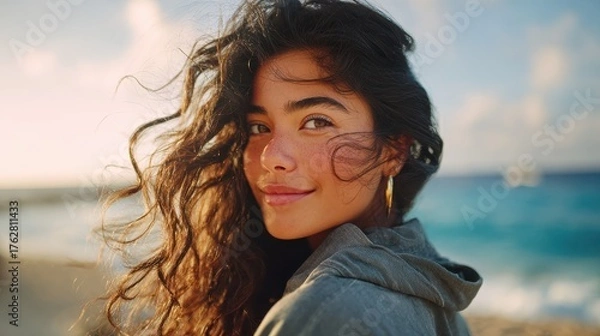 Fototapeta portrait of young woman at sea looking at camera smiling latin hispanic girl standing at the beach with copy space and looking at camera happy mixed race girl in casual outfit with wind in her hair n