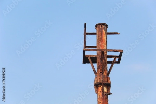 Fototapeta Close-up of an old rusty metal pole structure against clear blue sky. Industrial decay, weathered steel, and minimal composition showing texture, corrosion, and aging over time in outdoor environment