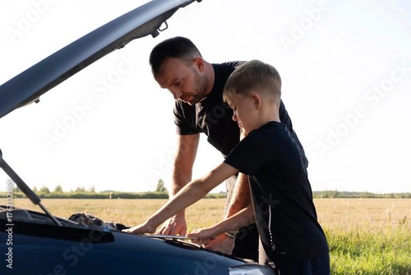 Fototapeta caring father teaches his beloved child how to repair car, explaining and teaching him how to use wrench and tools. They actively communicate while spending time together.