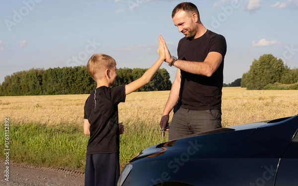 Fototapeta caring father teaches his beloved child how to repair car, explaining and teaching him how to use wrench and tools. They actively communicate while spending time together.