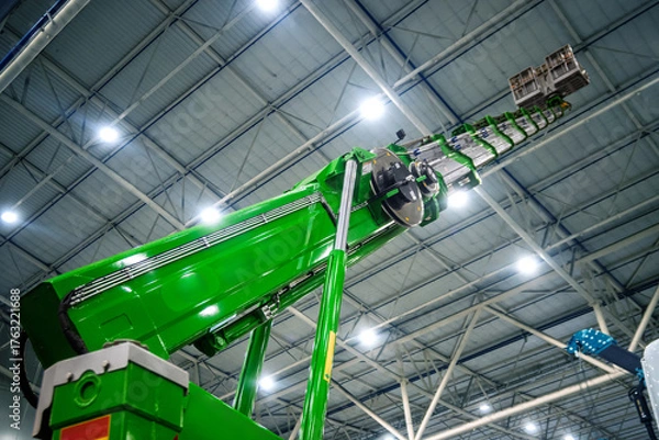 Fototapeta Modern bright green industrial machinery, a telescopic boom or crane, extending upwards in a high-tech factory or warehouse. Represents precision, innovation, and heavy industry.