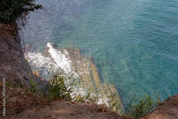 Fototapeta A view of a cliff on the seashore. Sea waves wash over the rocky shore.