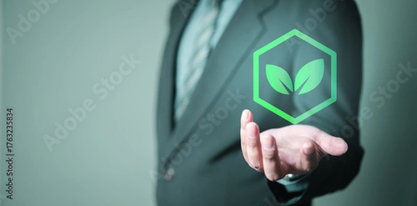 Fototapeta Businessman holding a green leaf icon, symbolizing carbon footprint tracking, sustainability, and eco-friendly initiatives to reduce emissions and promote environmental responsibility.