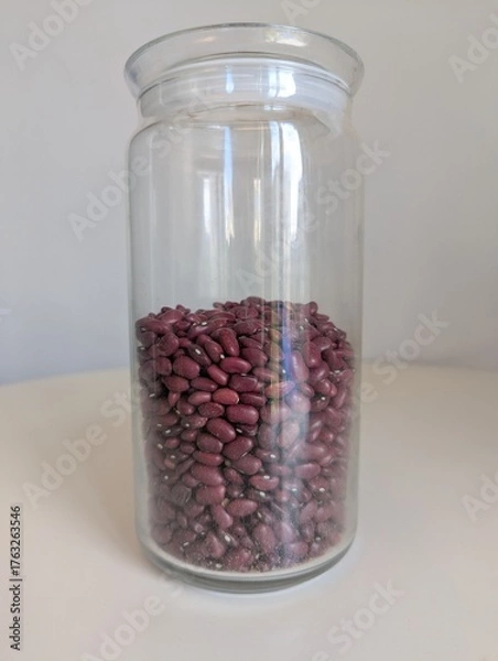 Fototapeta A half-full glass jar of red kidney beans, standing on a pristine white background. A simple, minimalist still life of a pantry staple.