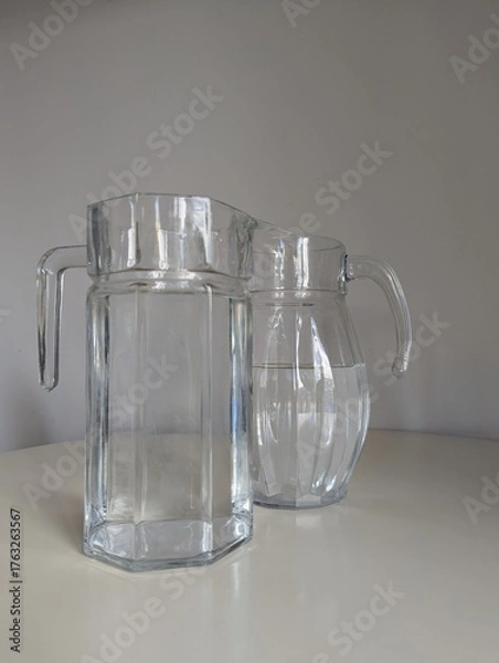 Fototapeta A pair of practical glass water pitchers for restaurant table settings, isolated together on a white background.
