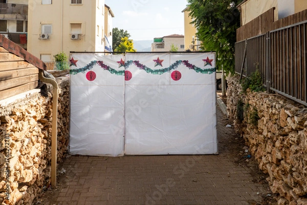 Fototapeta A sukkah stands in a narrow alley adorned with colorful decorations. This special structure is prepared for the Sukkot festival, inviting community celebrations.