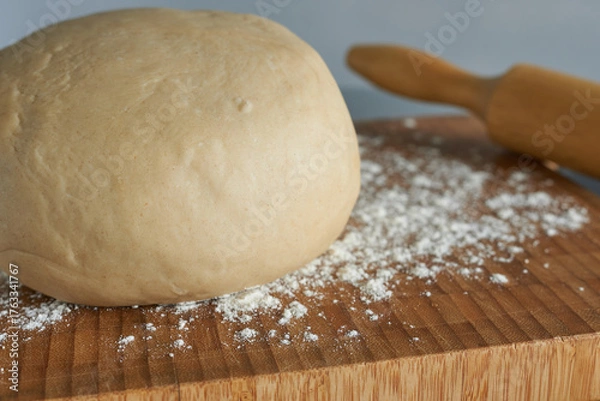 Fototapeta Close-up of dough. Yeast dough and rolling pin on a wooden cutting board.