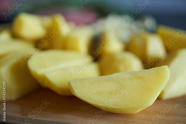 Fototapeta Raw potato slices, close-up, shallow depth of field. Potatoes cut into wedges on a cutting board.