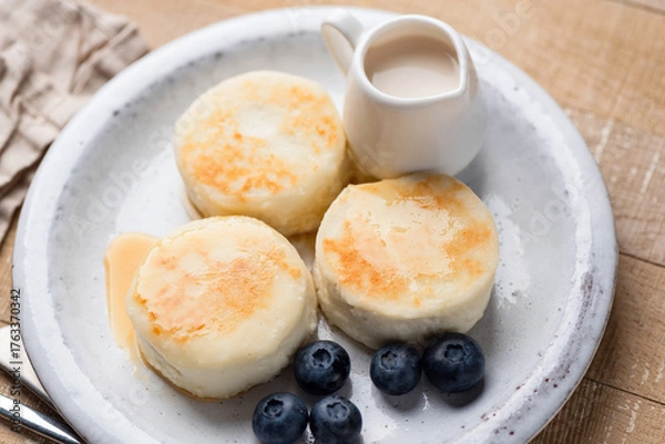 Fototapeta Syrniki, cottage cheese fritters served with blueberries, cream on a plate. Top view. Healthy breakfast meal