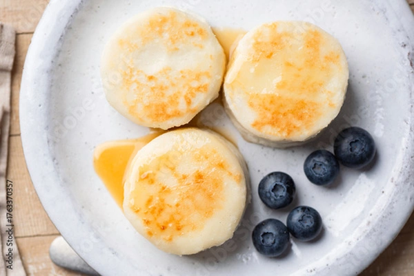 Fototapeta Syrniki, cottage cheese fritters served with blueberries, cream on a plate. Top view. Healthy breakfast meal
