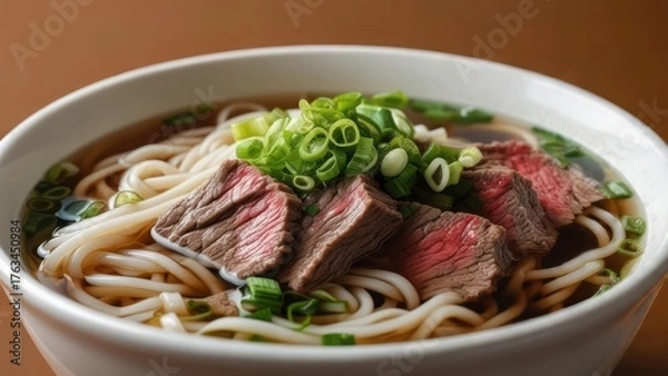 Obraz Steaming bowl of savory beef noodle soup topped with fresh green onions, a comforting and delicious meal perfect for any time.