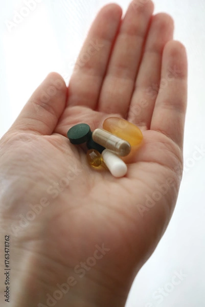 Fototapeta Close up of hand with various pills and capsules on white background. Dietary supplements and vitamins, treatment topic, pharmaceuticals, health improvement, vitamin deficiency in the human body.