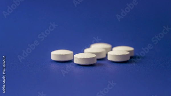 Fototapeta White round tablets scattered on a blue background highlighting the medication's simplicity and accessibility