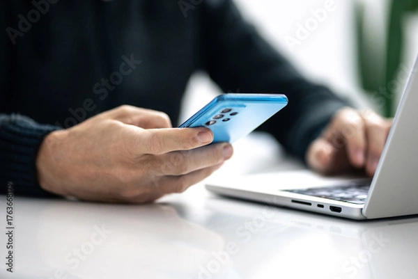 Fototapeta Closeup image of a male hands using smartphone and laptop. Boy working online, internet applications