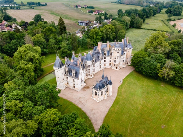 Fototapeta Aerial shot of Château de Meillant in Meillant, France, showing the château and its clear-standing chapel amid lush green fields and scattered trees.

