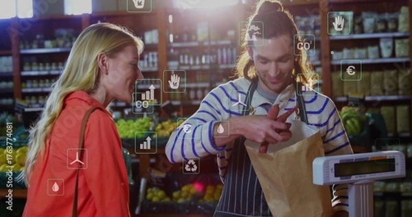 Fototapeta Packing clerk in apron placing red peppers into bag on scale in produce aisle, sustainability icons