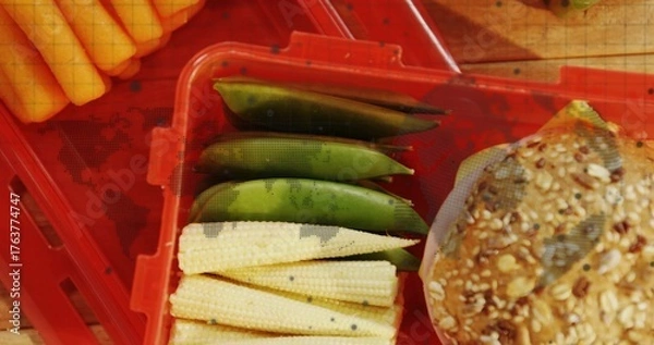 Fototapeta Resting red crate containing baby corn, sugar snap peas and seeded grain bun on kitchen countertop